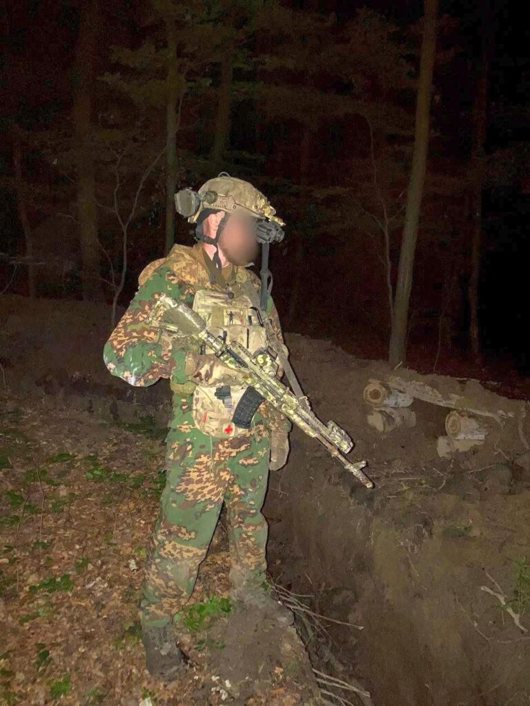 松林の塹壕線の隣で、「パルチザン」（レト）迷彩を着た（SSO）ウクライナ特殊作戦軍のオペレーターがライフルを構えた古い写真、2023年夏から秋。