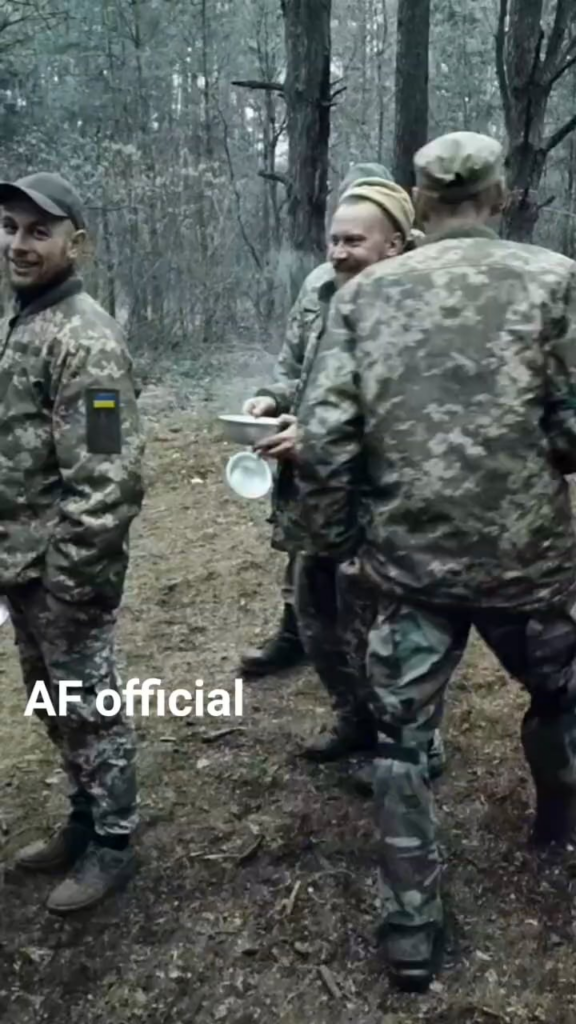 ウクライナ軍人たちは、森の中の野外キッチンで食事を求めて喜んで列をなしている。