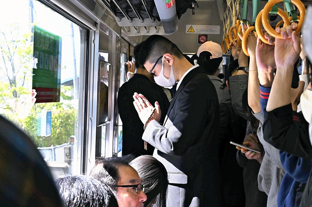 事故現場付近を通過する列車内で、手を合わせる乗客（２５日午前９時１６分、兵庫県尼崎市）＝代表撮影