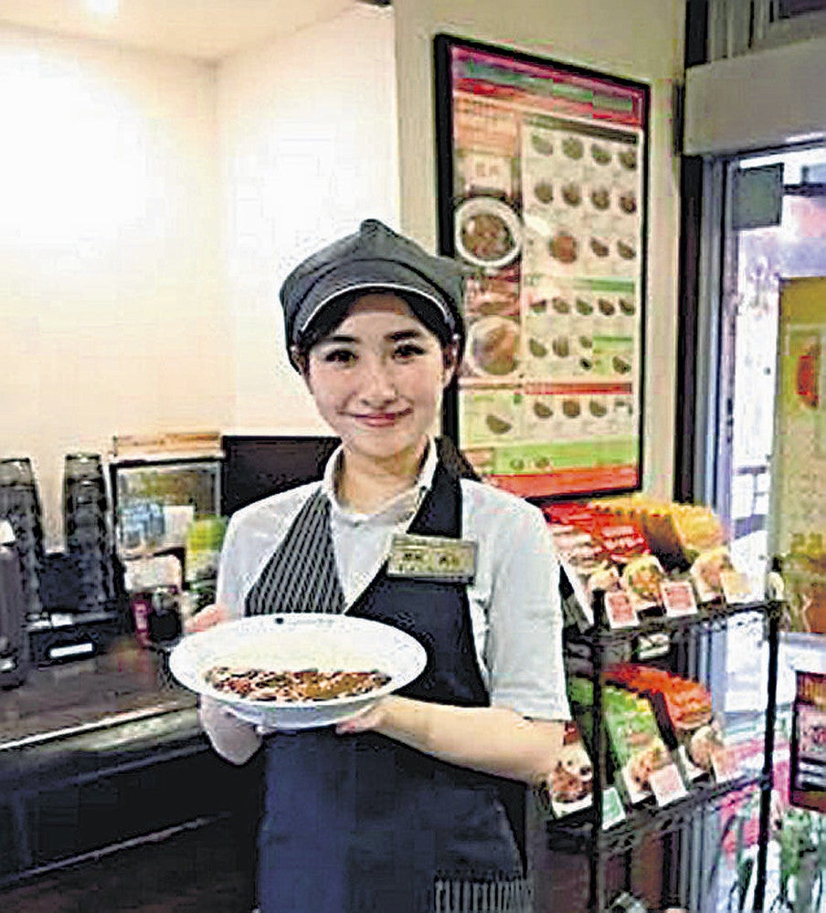 東京都内の店舗でカレーを掲げ、笑顔を見せる諸沢さん（スカイスクレイパー提供）
