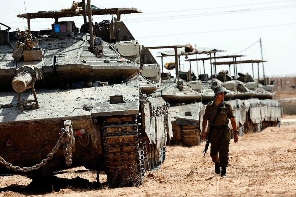 ２８日、イスラエルとガザの境界近くで、戦車のそばを歩くイスラエル兵＝ロイター