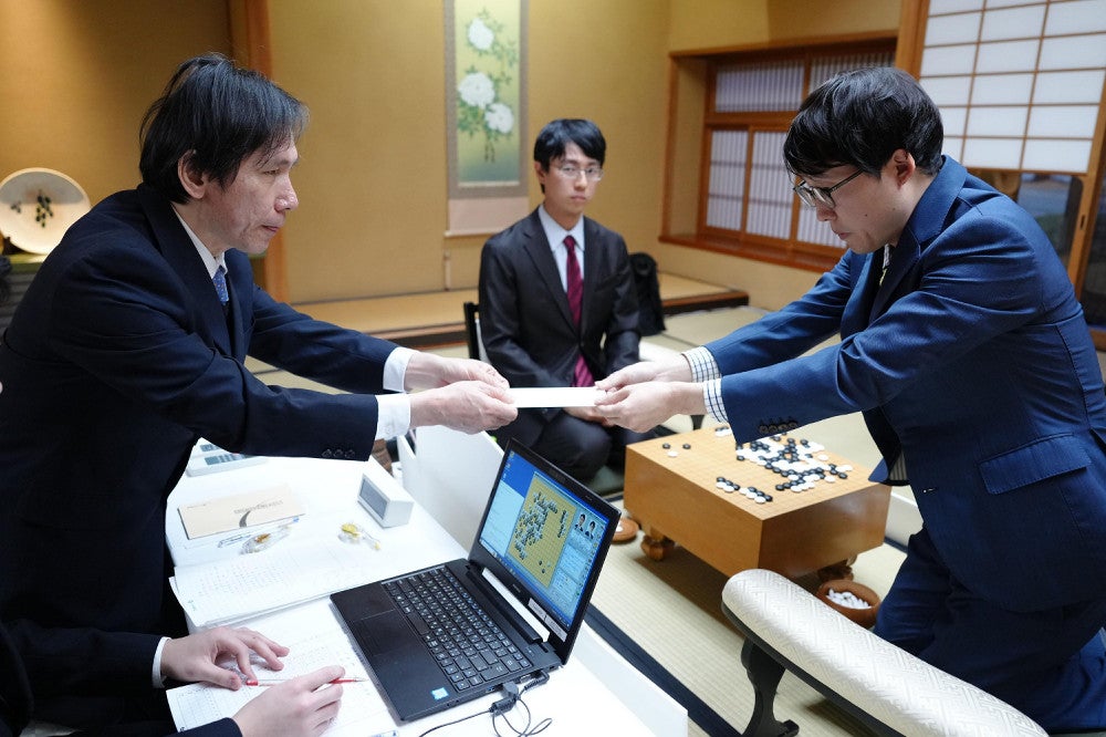 一力棋聖（中央奥）が見守る前で、封じ手の入った封筒を立会人の王銘琬九段に手渡す井山王座＝若杉和希撮影