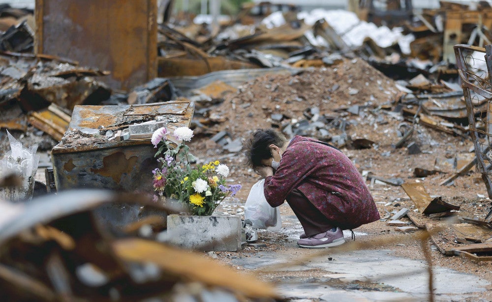火災で建物が焼け落ちた朝市通りで、犠牲になった知人を悼む女性（１日午後４時１３分、石川県輪島市で）＝片岡航希撮影
