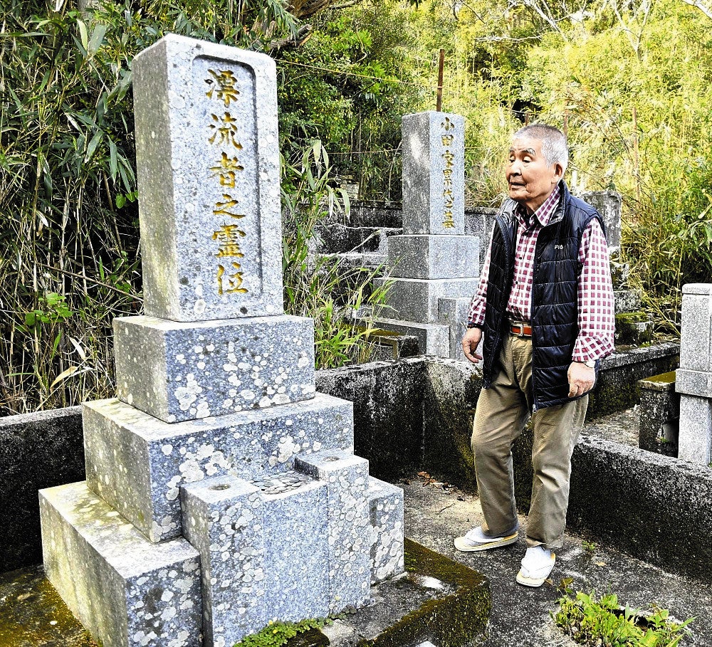 「漂流者之霊位」と刻んだ墓前に立つ宮川住職