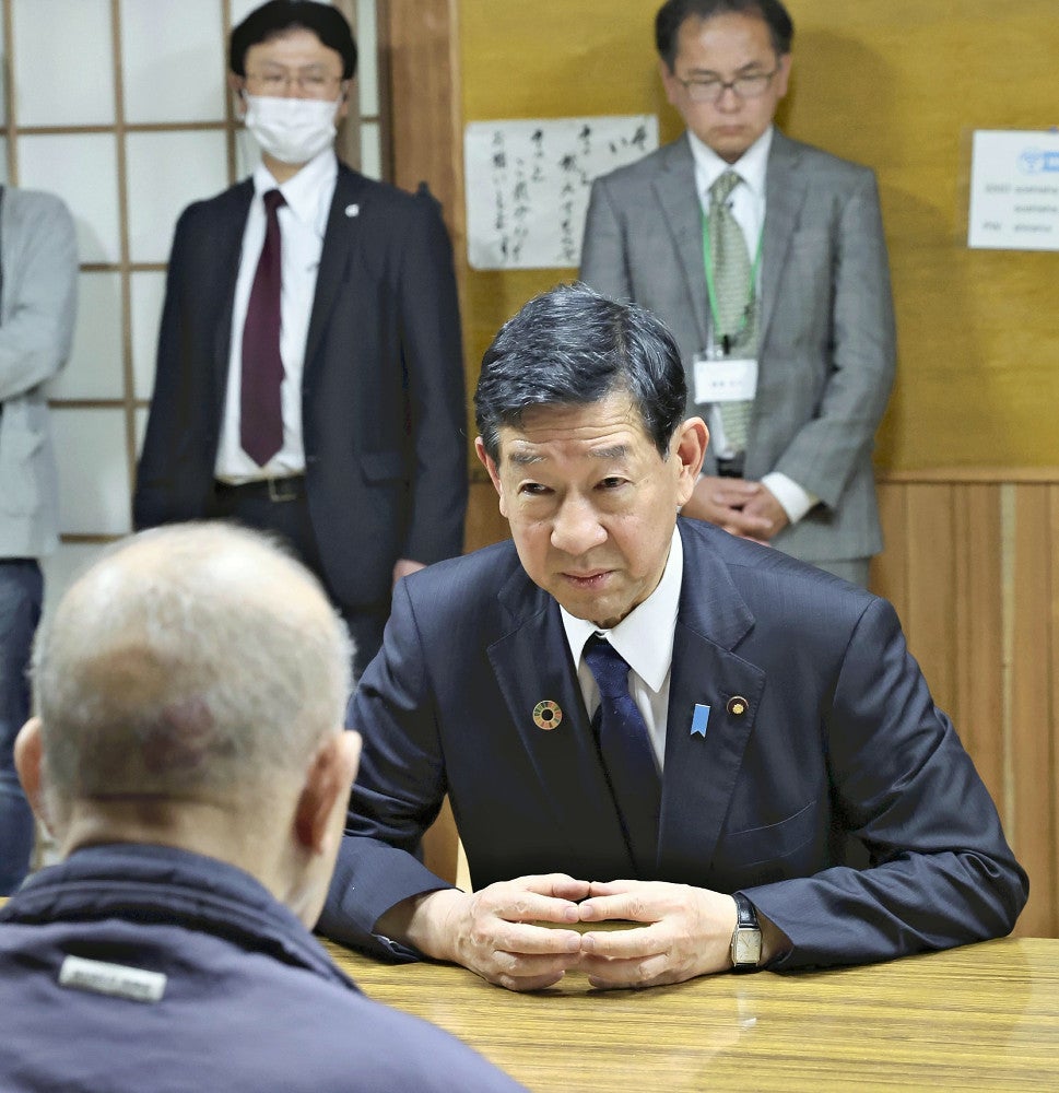 「水俣病患者連合」の松崎重光副会長（手前）の話を聞く伊藤環境相（８日、熊本県水俣市の水俣病センター相思社で）
