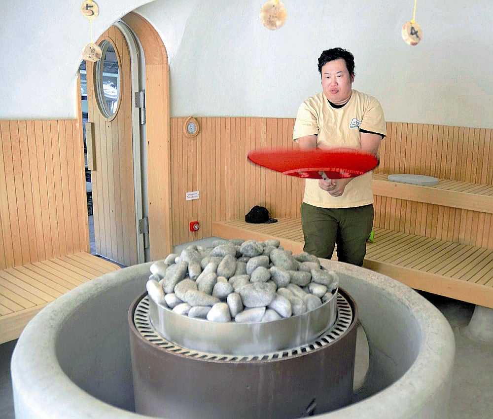 白を基調としたサウナ室で、うちわで熱波を送るサービスなどを担当する田中さん