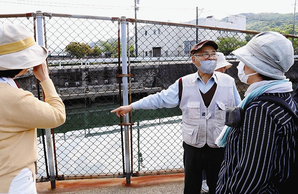 百間排水口（写真奥）について、山下さん（中央）から説明を受ける参加者たち（４月２８日、熊本県水俣市で）＝石原圭介撮影
