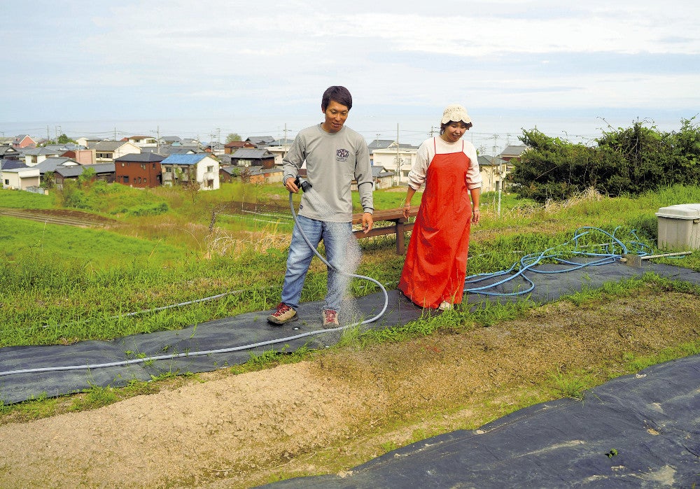 自宅近くの畑に水をまく草訳さん夫妻。眺望がお気に入りだという（兵庫県淡路市で）