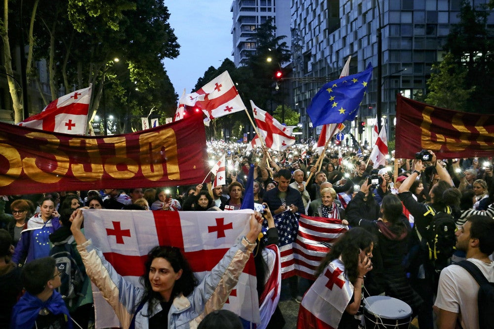 ２６日、ジョージアの首都トビリシで、米国とＥＵなどの旗を掲げ「外国の代理人」法案に抗議する人々＝ＡＰ