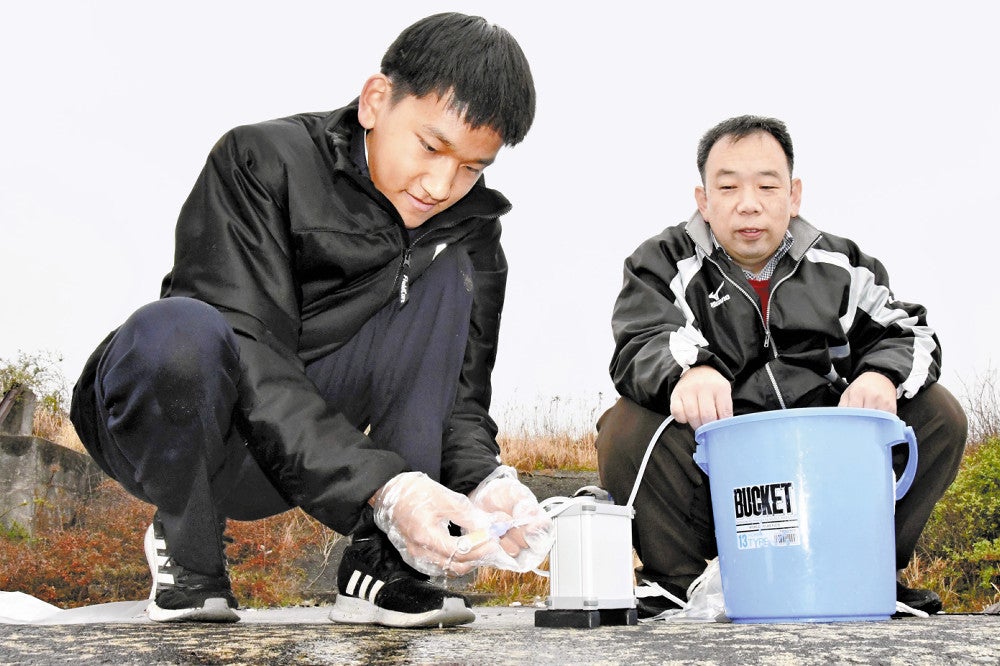 向教諭（右）の指導を受けながら、ポンプを使って川の水をこし取る松本さん（３月１７日、福岡県みやま市で）