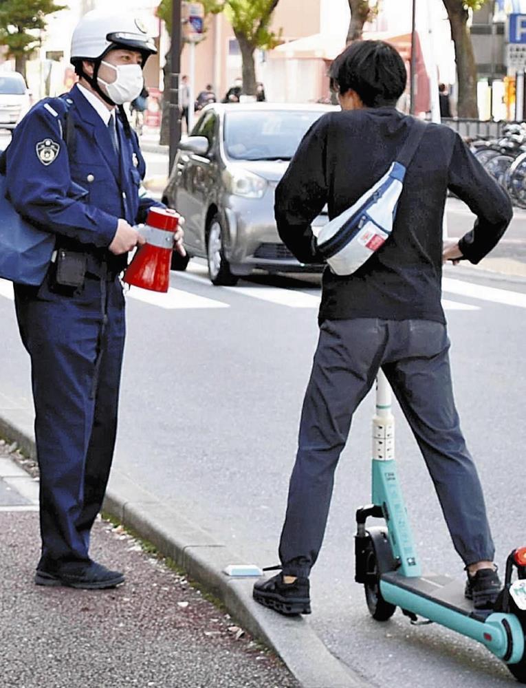電動キックスケーターの利用者に安全運転を呼びかける福岡県警南署員（４月５日、福岡市南区で）