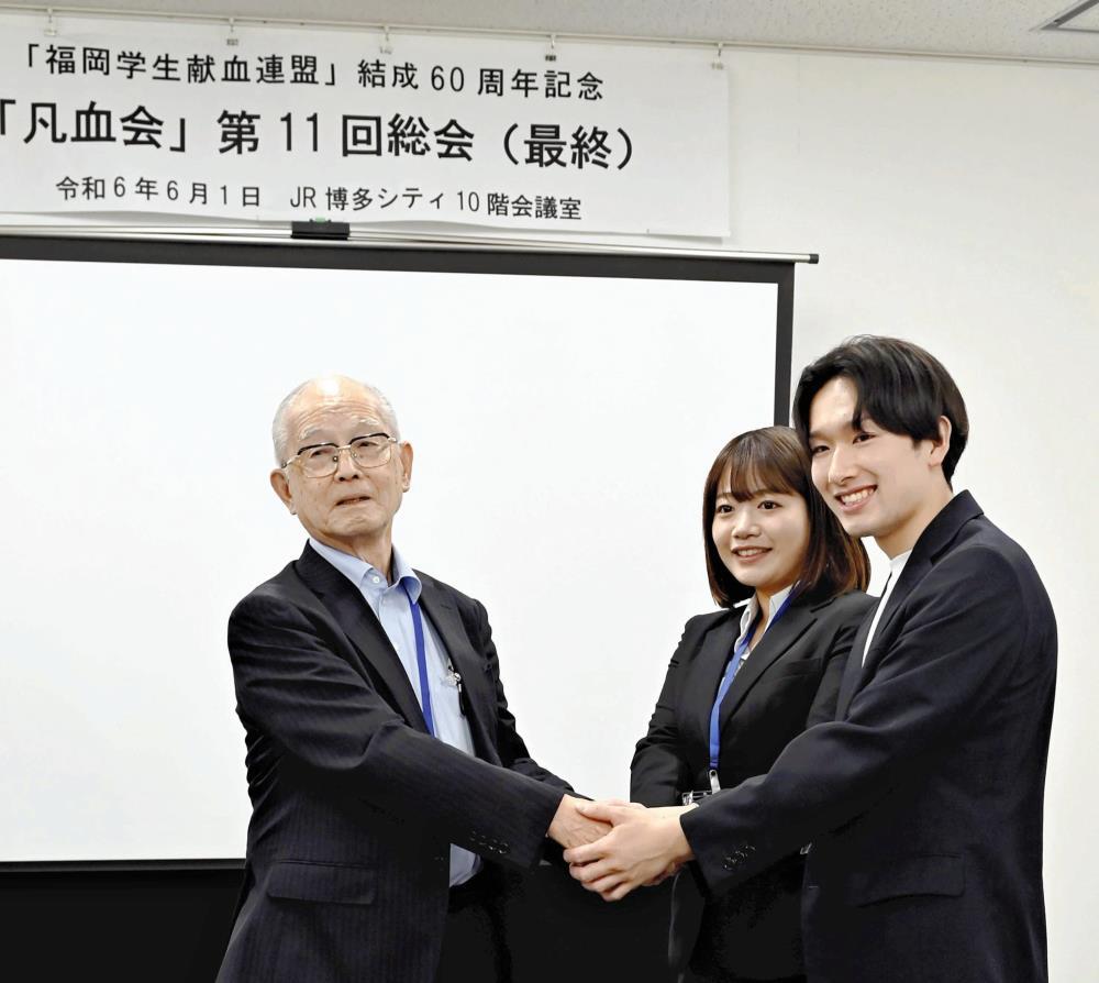 現在の献血運動を担う「福岡学生献血推進協議会」の大学生と握手を交わす田中さん（左）