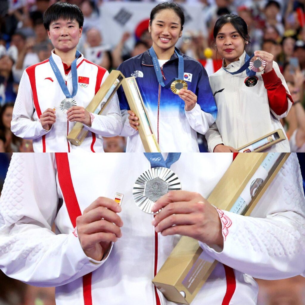 中国のシャトル選手、何冰嬌は、スペインの準決勝の対戦相手が負傷で棄権した後、スペイン国旗のバッジを持って表彰台に上がった。