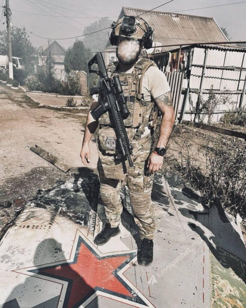 墜落したS-70「ハンター」ジェット無人機の上で写真を撮るウクライナ兵士。場所不明 - 2024 年 10 月