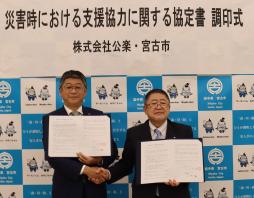 調印式で山田代表取締役と山本宮古市長が右手で握手をし、協定書を見せながら記念撮影をしている写真