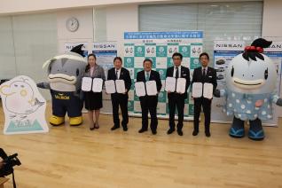 キャラクターマスコットに挟まれ女性1名と男性4名が協定書を両手にもち記念撮影をしている写真