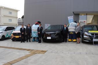 右から2台目の黒い車の両端に並んで記念撮影をしている関係者5名の写真