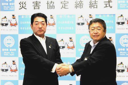 久保憲雄組合長と山本宮古市長が両手で握手をして記念撮影をしている写真