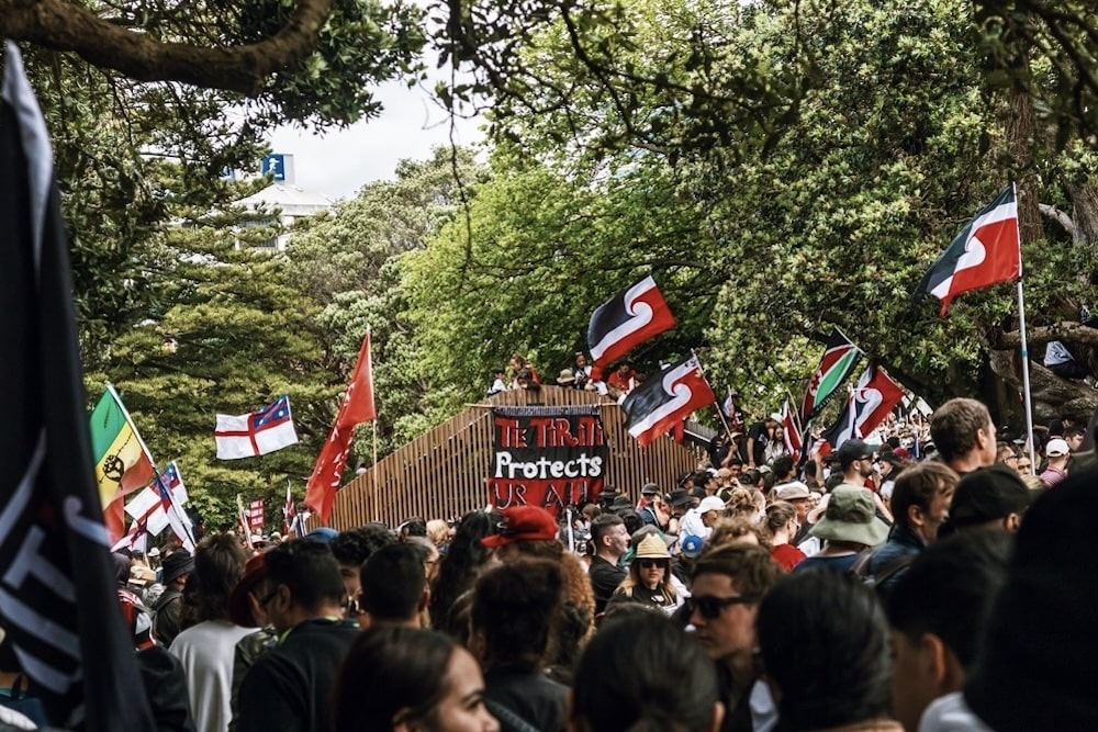 マオリの赤と黒の旗を掲げて歩く大勢の人