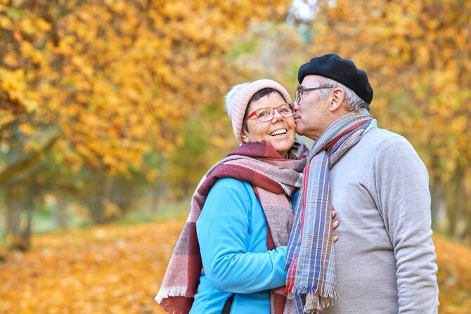 秋の公園で妻にキスをする年配の男性