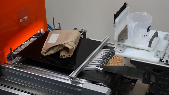 プラティパスビジョンが開発した穀物品質検査装備が稼動している。 右側に投入された小麦粒がコンベヤーベルトに乗って左側に移動し、赤色部分の中に設置されたカメラを通じてAIで分析する方式だ。