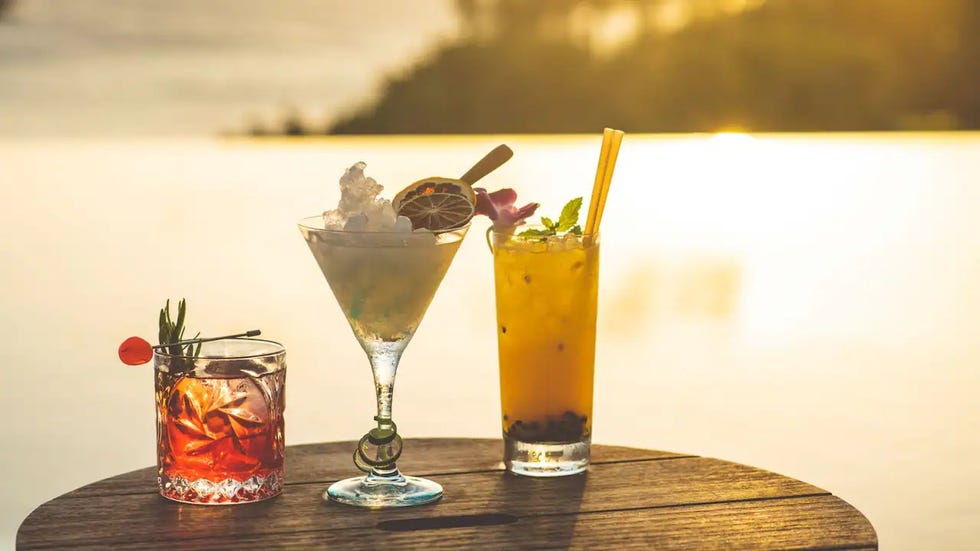 assortment of three vibrant cocktails on a wooden table with a scenic backdrop