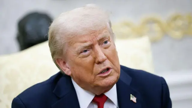 ダークスーツ、白いシャツ、赤系のネクタイを着けたトランプ大統領が口を少し開いて前方を見ている