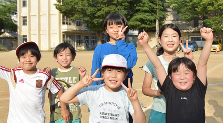 校庭で男の子と女の子がピースサインや両手を上に上げてポーズをとっている写真