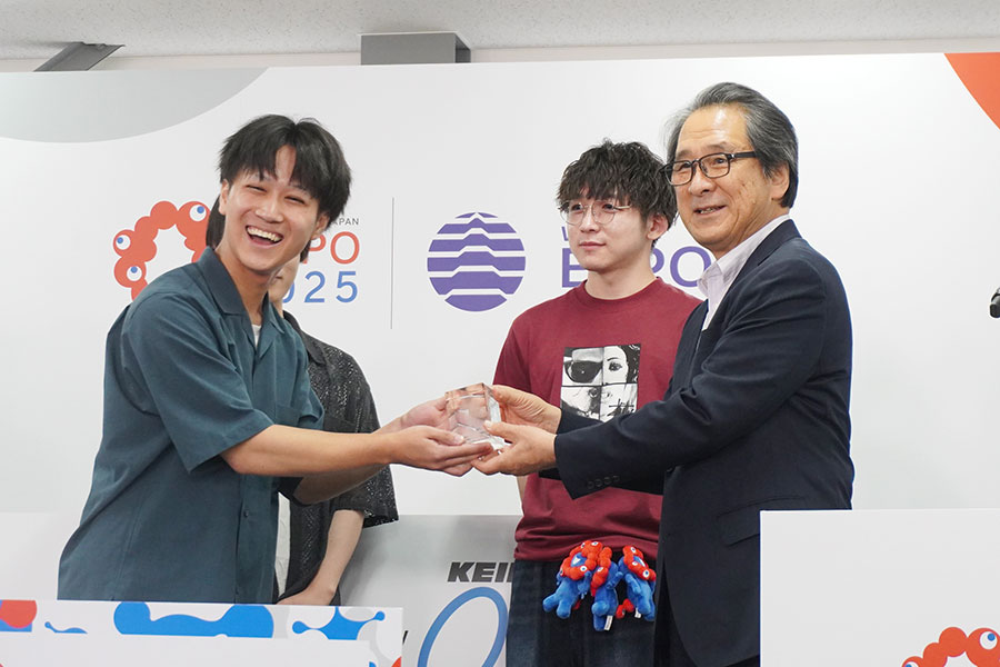 2025万人突破を記念したセレモニーの様子。石毛会長から贈呈された記念品を満面の笑みで受け取る徳丸さん（9月6日／大阪・関西万博）