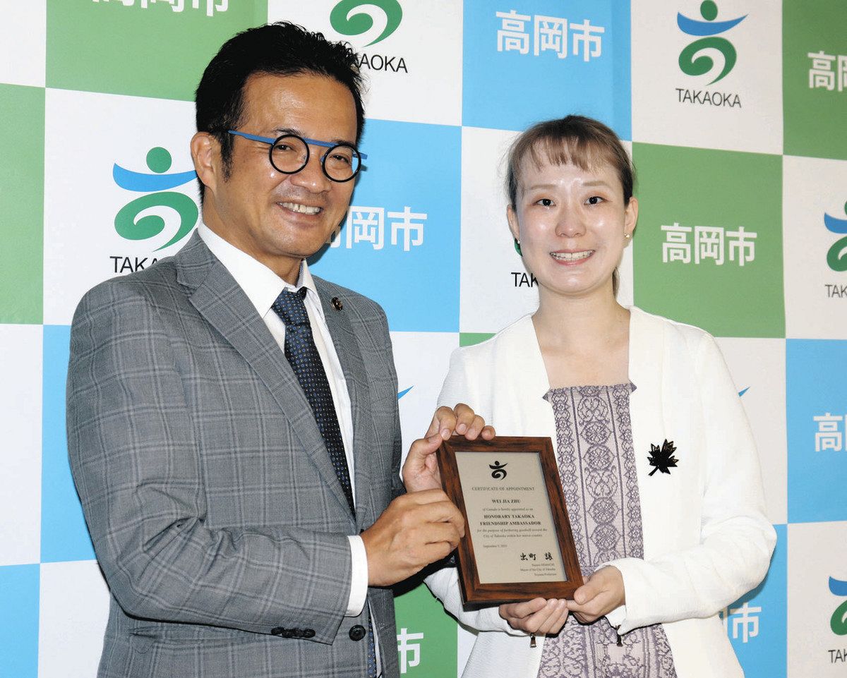 出町譲市長（左）から盾を受け取るウェイジア・ジュウさん。胸元のメープルの葉の形のブローチは高岡漆器で、市民からもらった＝高岡市役所で
