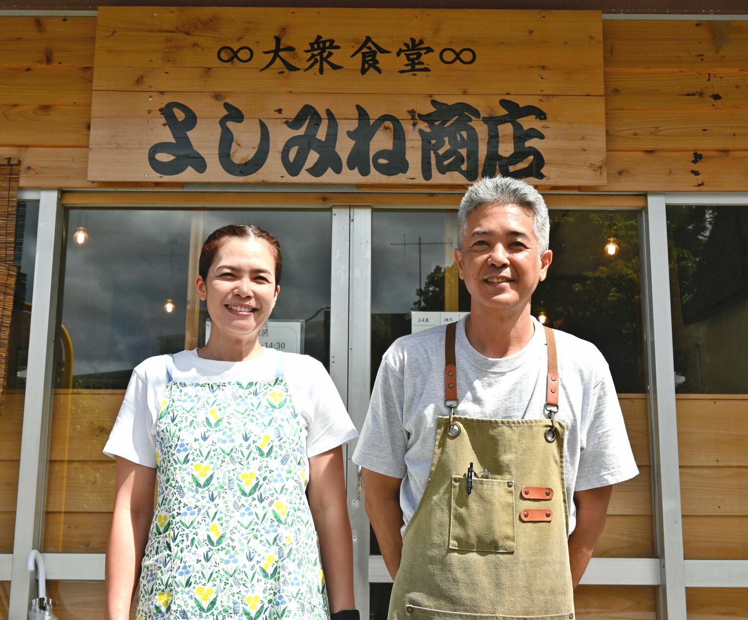 祖父母から受け継いだ「よしみね商店」の看板の前で笑顔の並里盛司さん（右）と妹の金城律子さん＝１日、那覇市繁多川
