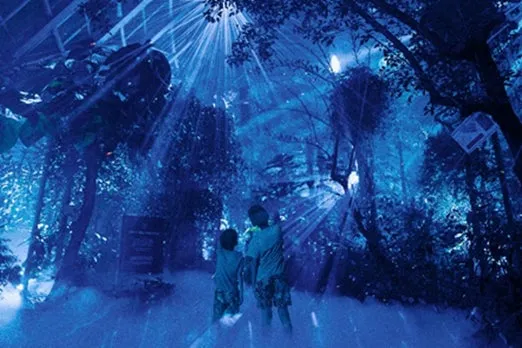 青い光の中に立つ2人の子供の画像です。光は上から差し込み、木々を照らしています。子供たちは光を見上げています。