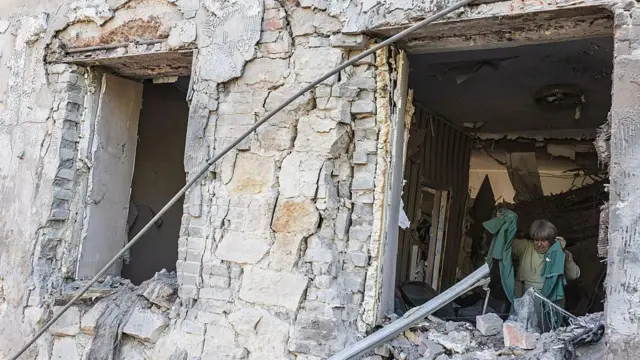 ロシア軍の攻撃でひどく損傷した石造りの住宅の中で、女性が洋服などを持ち上げている（ウクライナ東部ドネツク州ドルジキウカ）