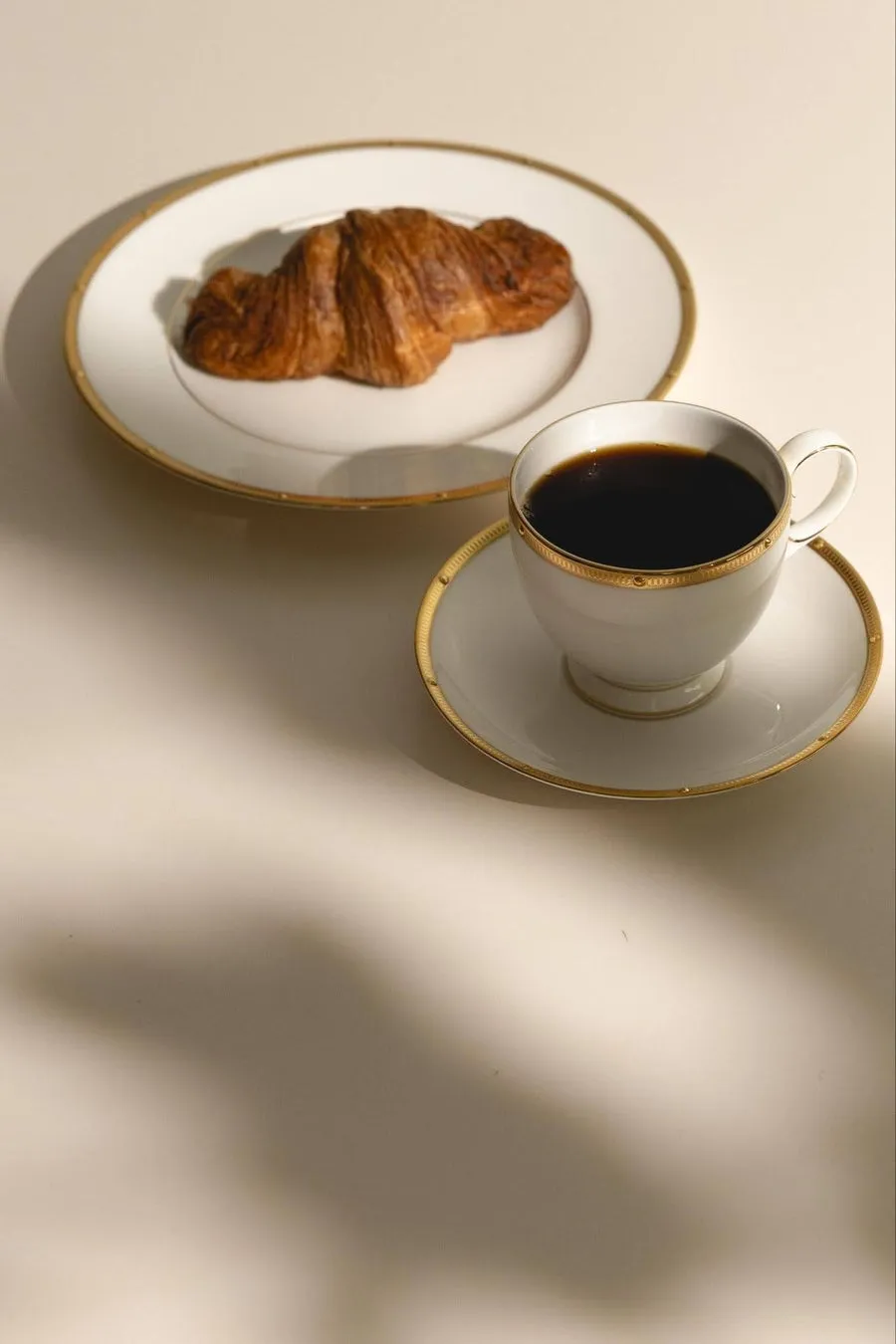 クロワッサンとコーヒーの入ったカップが置かれた、上品な朝食の様子を捉えた写真です。白と金色の縁取りが施された食器が、洗練された雰囲気を醸し出しています。