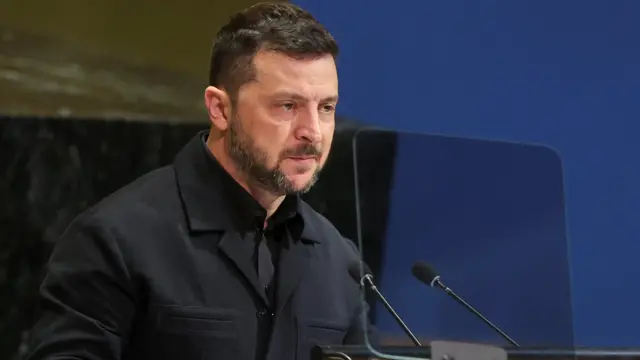 黒いジャケットとシャツを着たウクライナのゼレンスキー大統領が険しい表情で、マイクに向かって話している