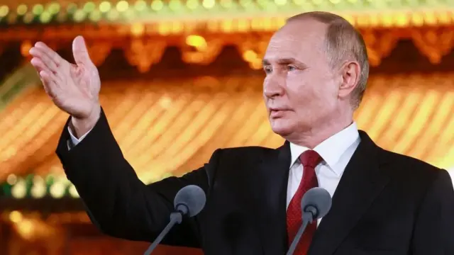 ダークスーツに白いシャツ、赤いネクタイを締めたプーチン大統領が、2本のマイクが置かれた演壇の前で右手を広げ、記者団の質問に答えている
