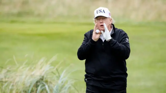 ゴルフ場の芝の上に、白いキャップと黒いゴルフウェアで立つトランプ氏。キャップには「USA」と書かれている。ゴルフボールを右手に、左手に白い手袋をしたトランプ氏は両手で口元を挟み、声を出している