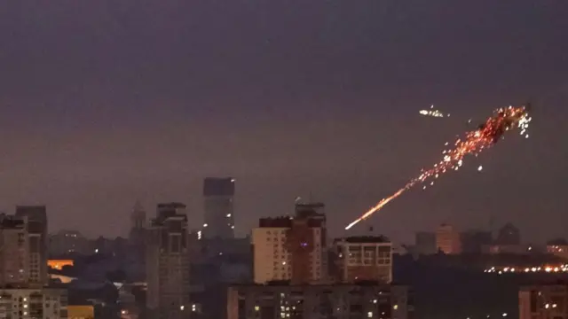 キーウの夜空を背景に、上空で迎撃されたドローンからオレンジと白の火花が噴き出している