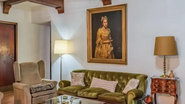 リビングルームの白い壁に女性の肖像画が掛けられている。壁の前には緑色のソファが置かれ、両側にはランプが一つずつ置かれている