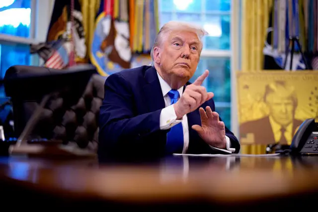 ホワイトハウスの大統領執務室で机に座るドナルド・トランプ大統領。向かい側にいる人物を指さして話しかけようとしているように見える