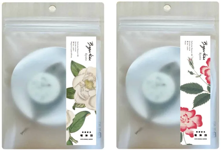 白を基調とした香水瓶のようなものと、花のイラストが描かれたラベルが特徴的な商品の写真。透明な袋に入っており、エレガントな印象を与えます。