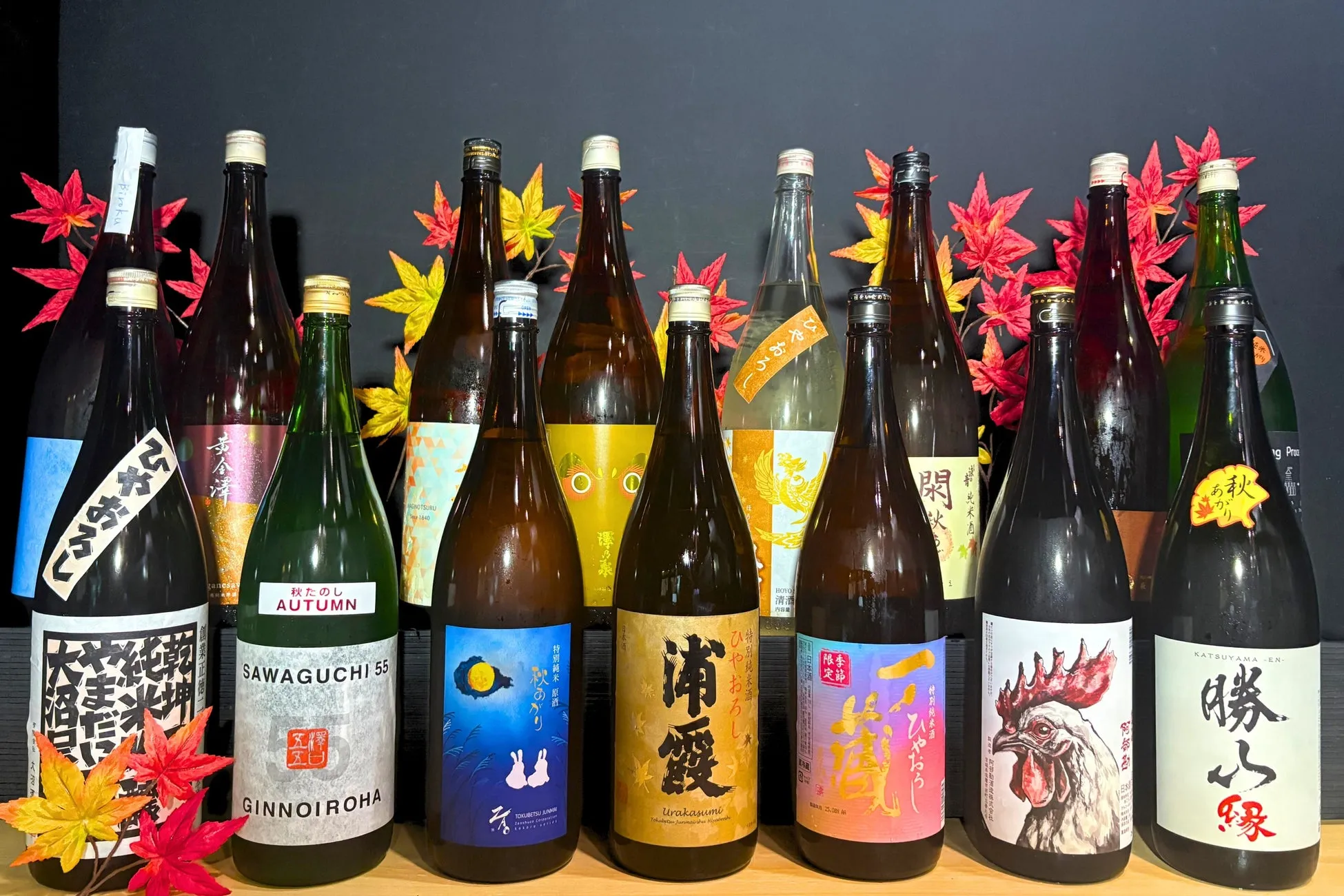 様々なお酒の瓶が並んだ写真。秋をテーマにした装飾が施されており、日本酒のラベルが特徴的。