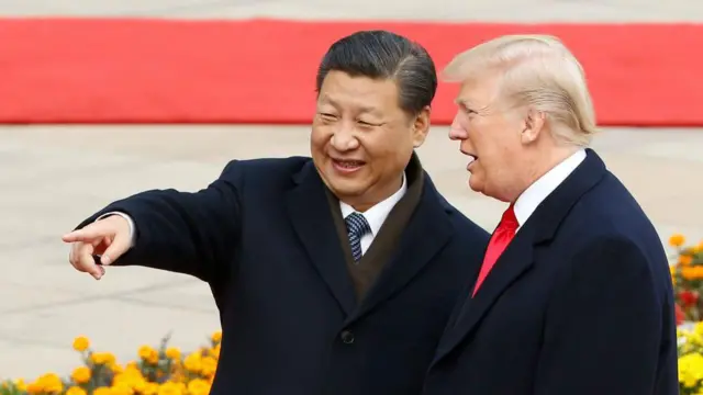 中国の習近平中国国家主席と並んで会話するドナルド・トランプ米大統領。習氏は左側を指さしてトランプ氏に何かを示している。場所は式典会場のようで、背後に赤いじゅうたんと花が見える