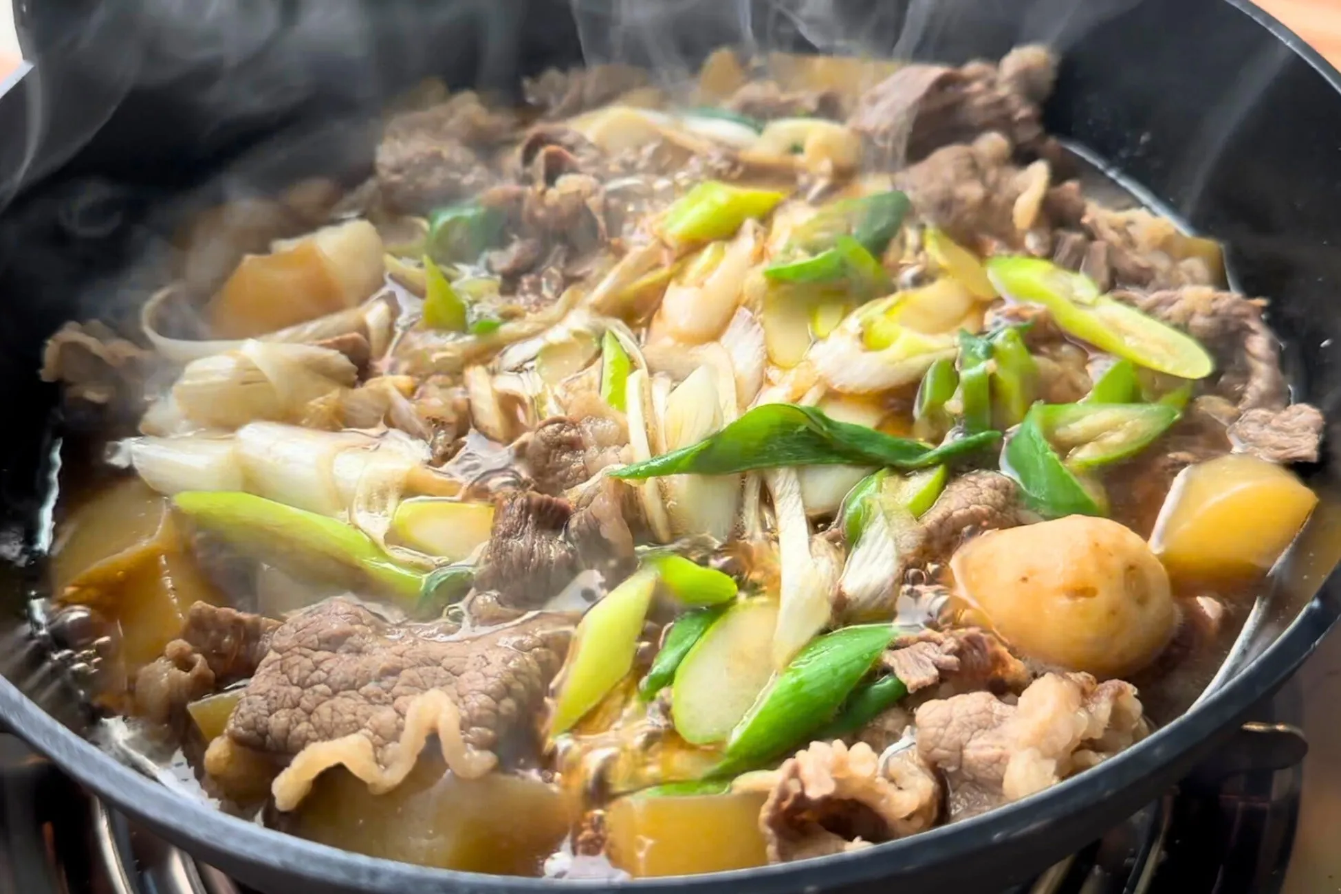 鍋料理の写真。牛肉、ネギ、ジャガイモなどが入っていて、湯気が立っている。