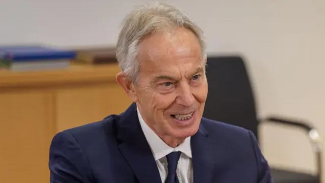 紺のスーツとネクタイ姿、白髪のブレア元英首相が笑顔で話している