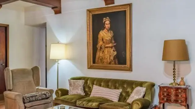 リビングルームの白い壁に女性の肖像画が掛けられている。壁の前には緑色のソファが置かれ、両側にはランプが一つずつ置かれている