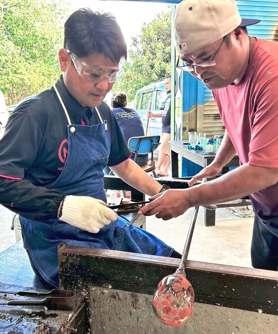 現地職人のサポートを受け吹きガラス体験をする高山博明教諭（左）＝８月５日、パラオのベラウ・エコグラスセンター