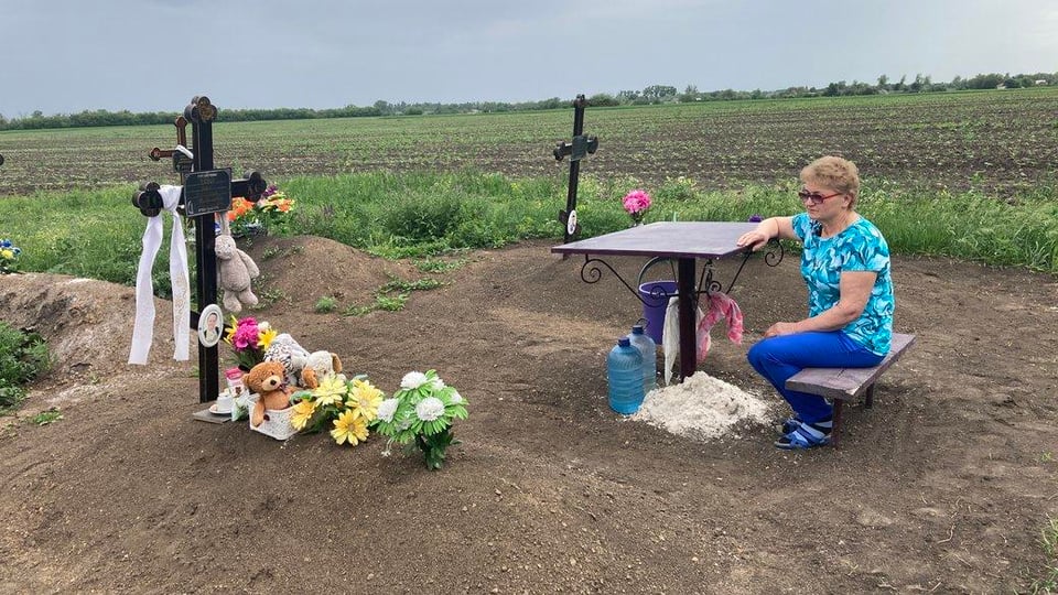 8歳の孫イワン君の墓に座る女性。彼女はまた、ロシアのストライキで子供たちと夫を亡くした。