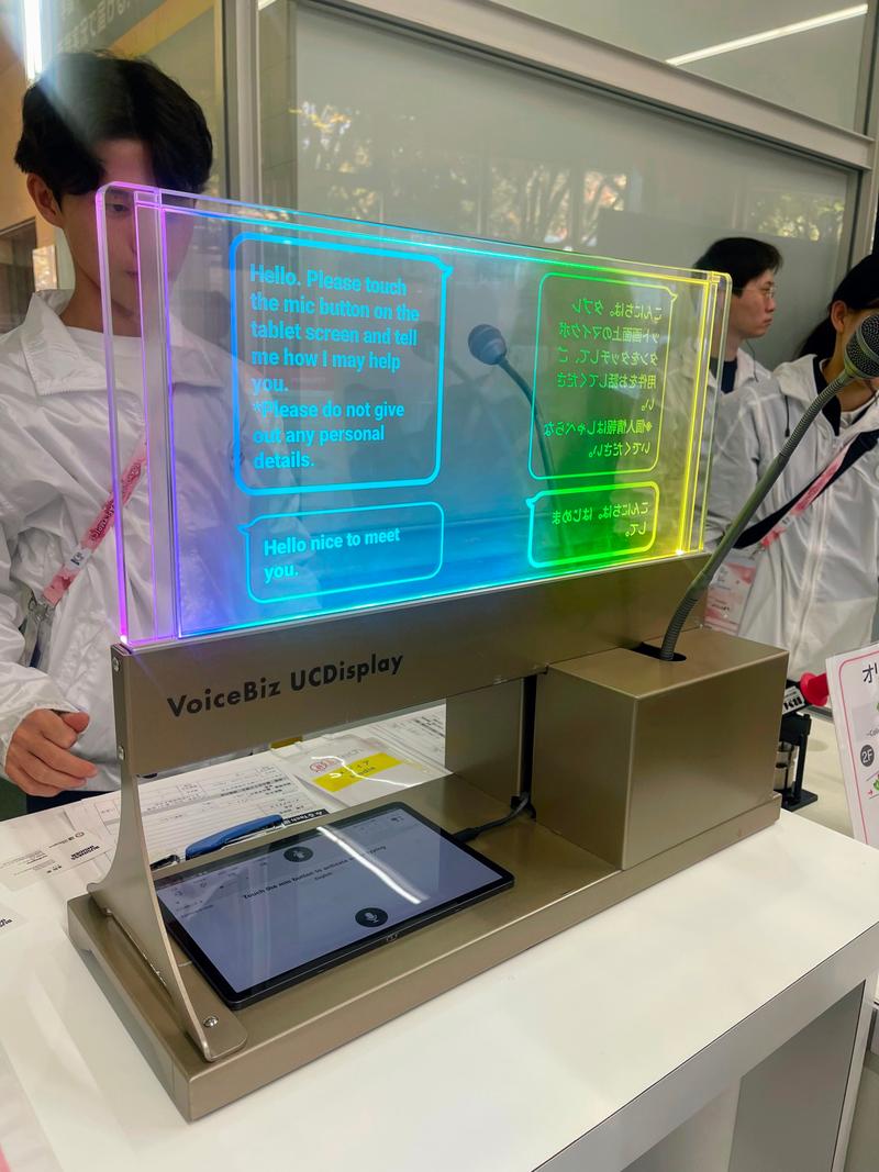 会場受付に設置されているTOPPANが開発した「VoiceBiz® UCDisplay®」。音声またはキーボード入力した内容の翻訳結果が透明なディスプレイに表示され、相手の顔を見ながら会話することができる。 