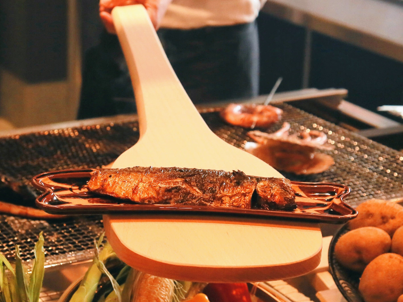 炭火で香ばしく焼き上げた料理を、大きなしゃもじで提供